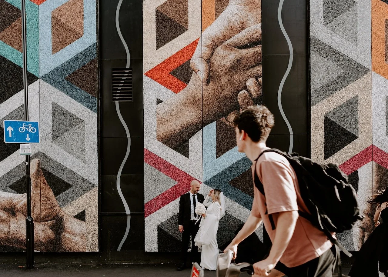 Bride and groom standing in front of colourful street art mural in London as a cyclist passes by