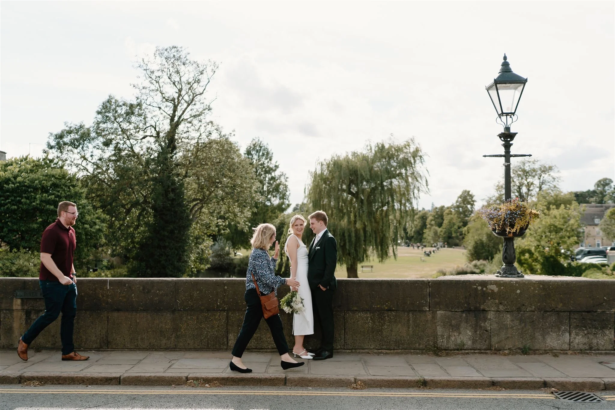 Bride and groom standing on a bridge in Stamford near the George Hotel while people walk past.
