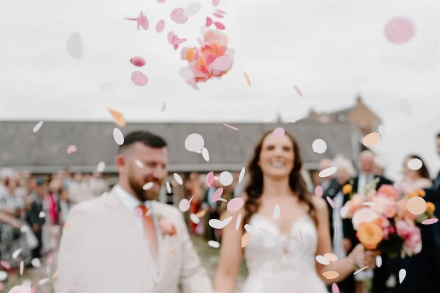 Documentary wedding photograph of colourful confetti being thrown over a newly married couple as they walk back down the aisle
