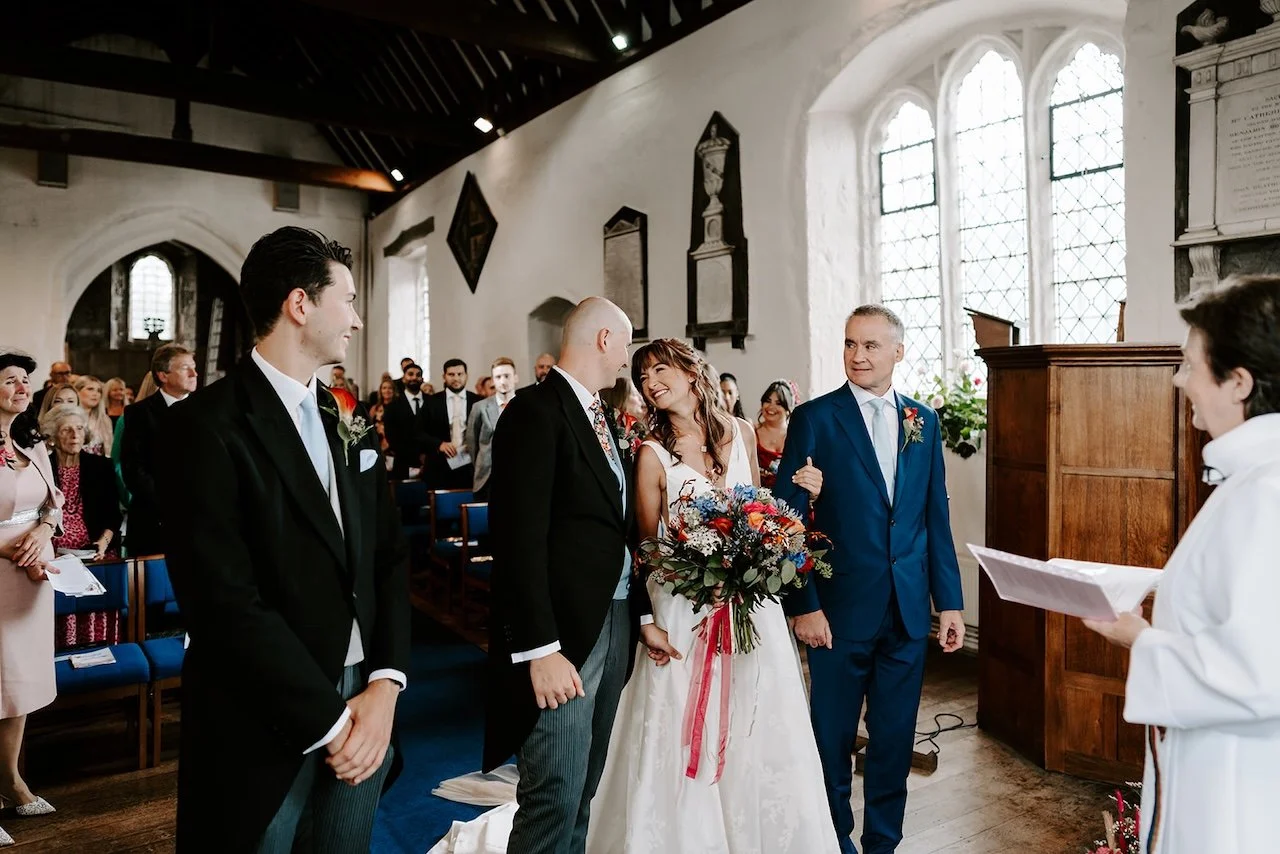 Bride walking down the aisle at Chingford church in East London, smiling at her partner as guests watch during the wedding ceremony.