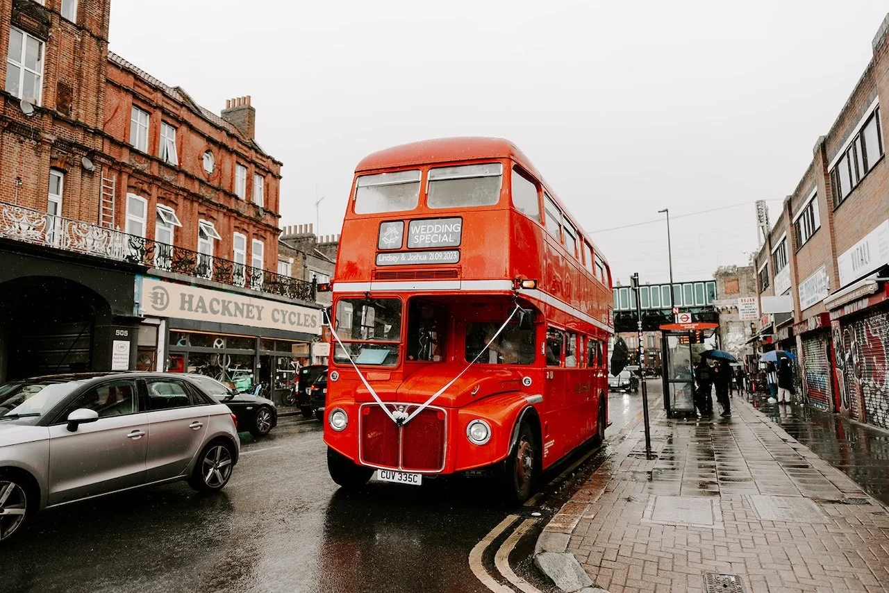 Red London double decker wedding bus arriving on Hackney Road in East London on a rainy day, transporting guests to The Hackney venue