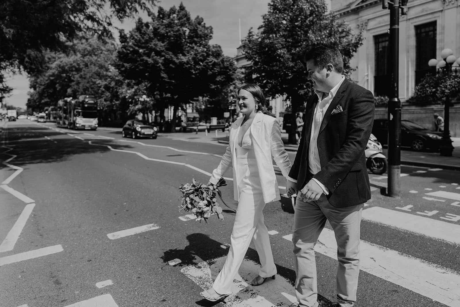 Bride in a white jumpsuit crossing a London road with her partner after their town hall ceremony
