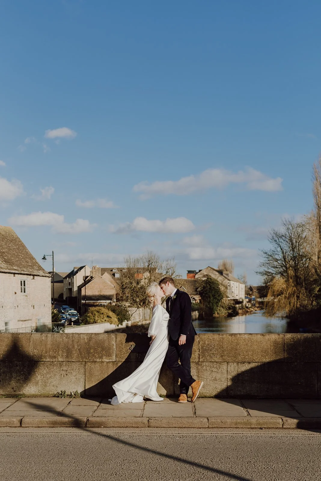 Bride and groom kissing on a stone bridge in Stamford with the River Welland behind them