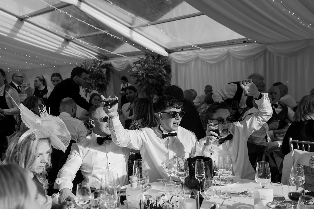 Wedding guests in black tie celebrating and cheering during speeches inside the marquee at Exton Park.