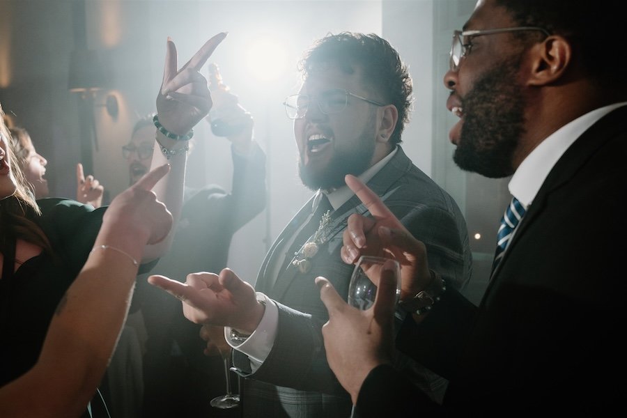 Documentary wedding photograph of guests singing on a packed dance floor with hands pointing towards the centre