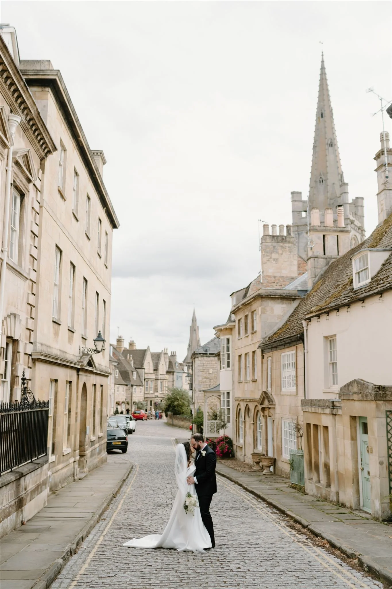 Bride and groom embracing in the middle of Barn Hill in Stamford, framed by historic stone buildings and church spires