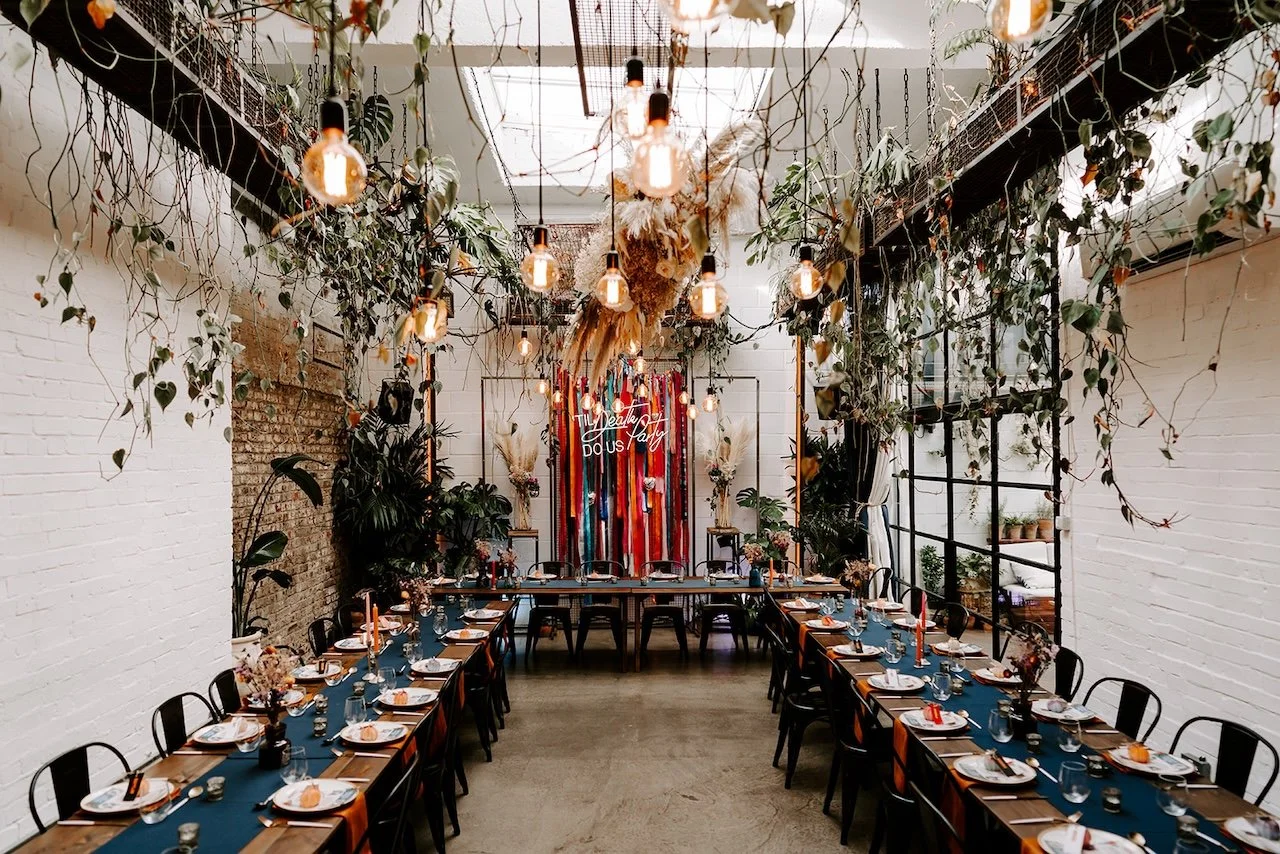 Long dining tables set for a wedding reception at The Hackney, with hanging plants, exposed brick walls and warm festoon lighting in East London.