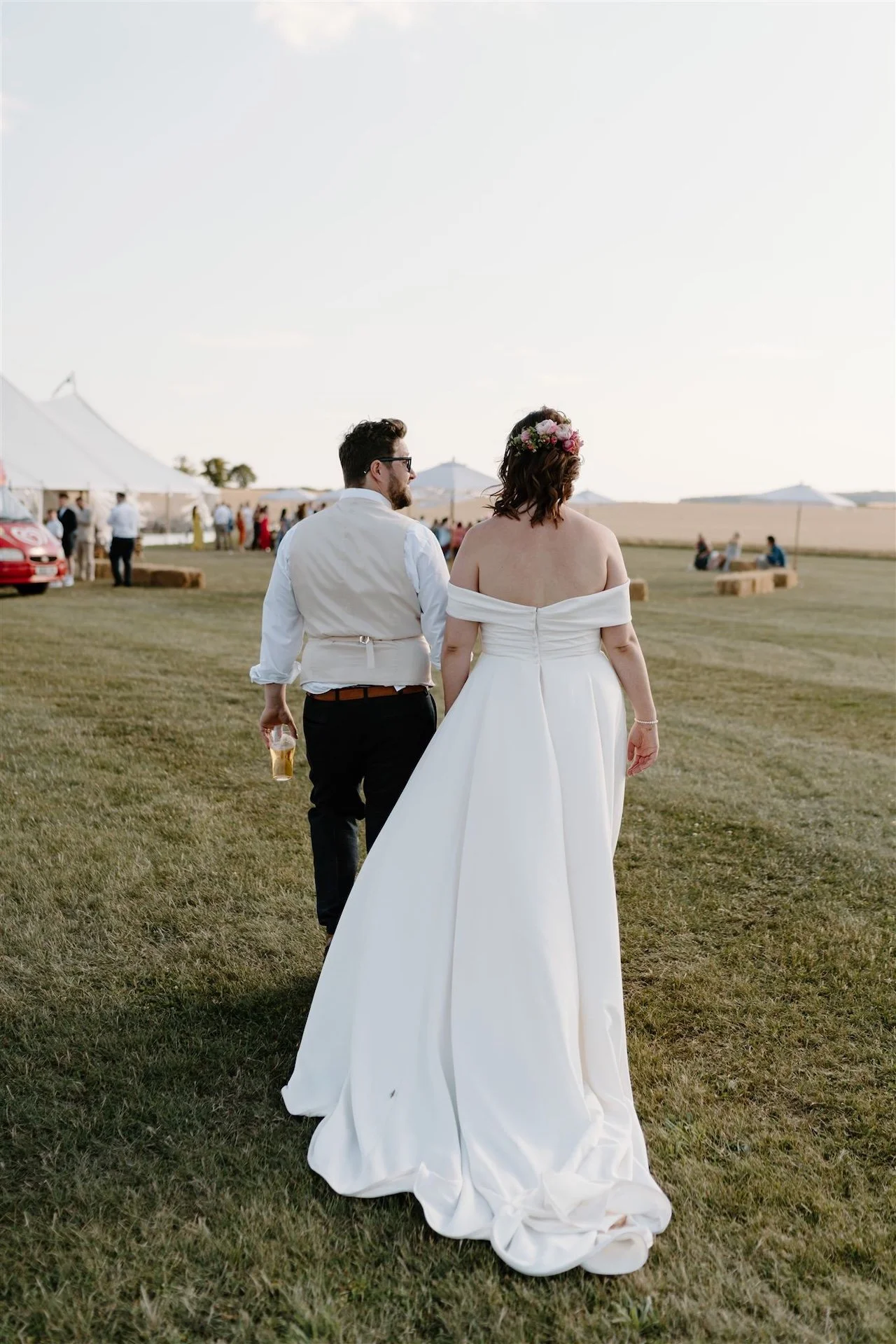 Bride and groom walking hand in hand across a field towards a marquee at Ed’s Hilltop Tent near Stamford.