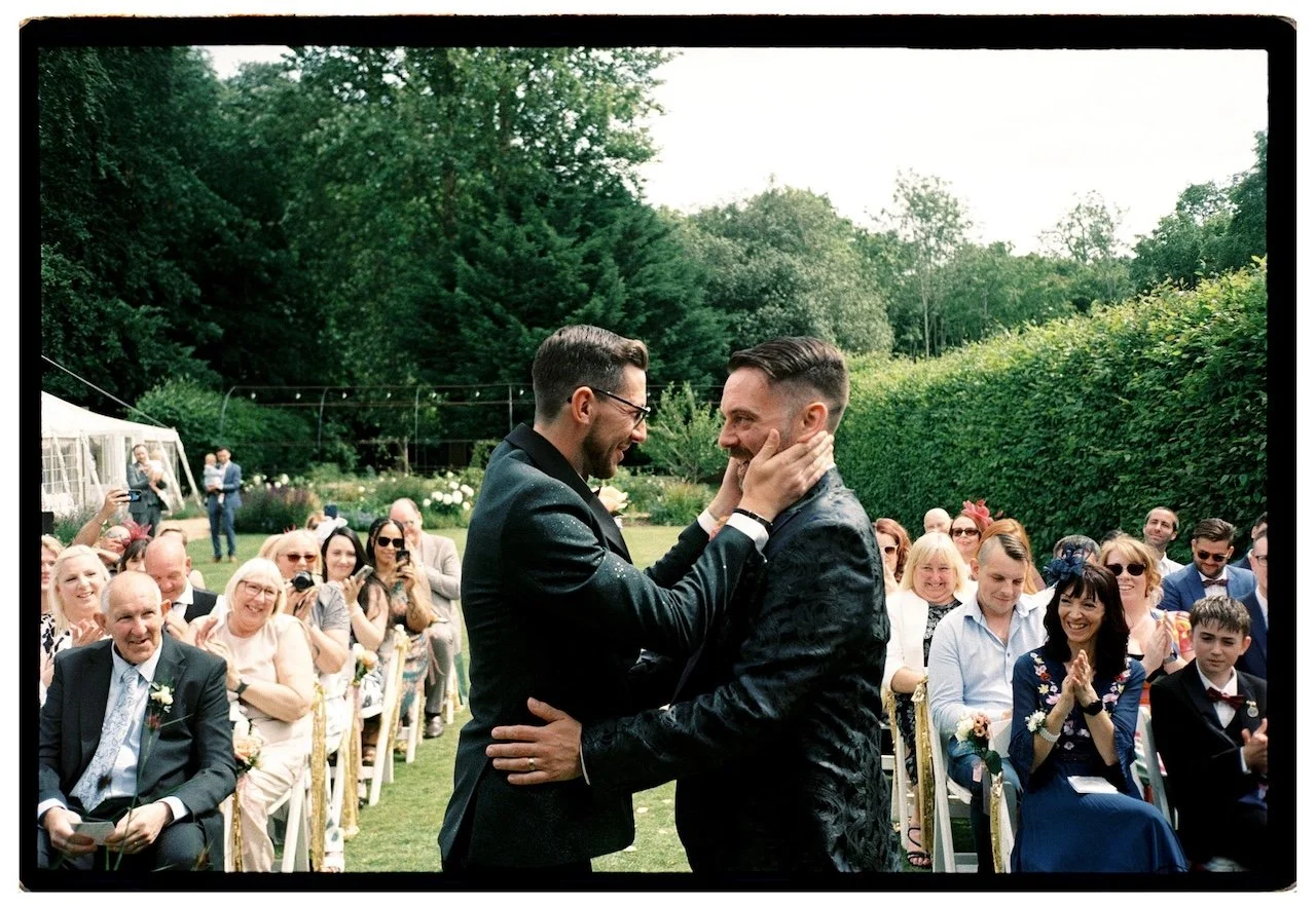 Two grooms sharing a moment during an outdoor ceremony at The William Cecil in Stamford, intimate documentary wedding photography