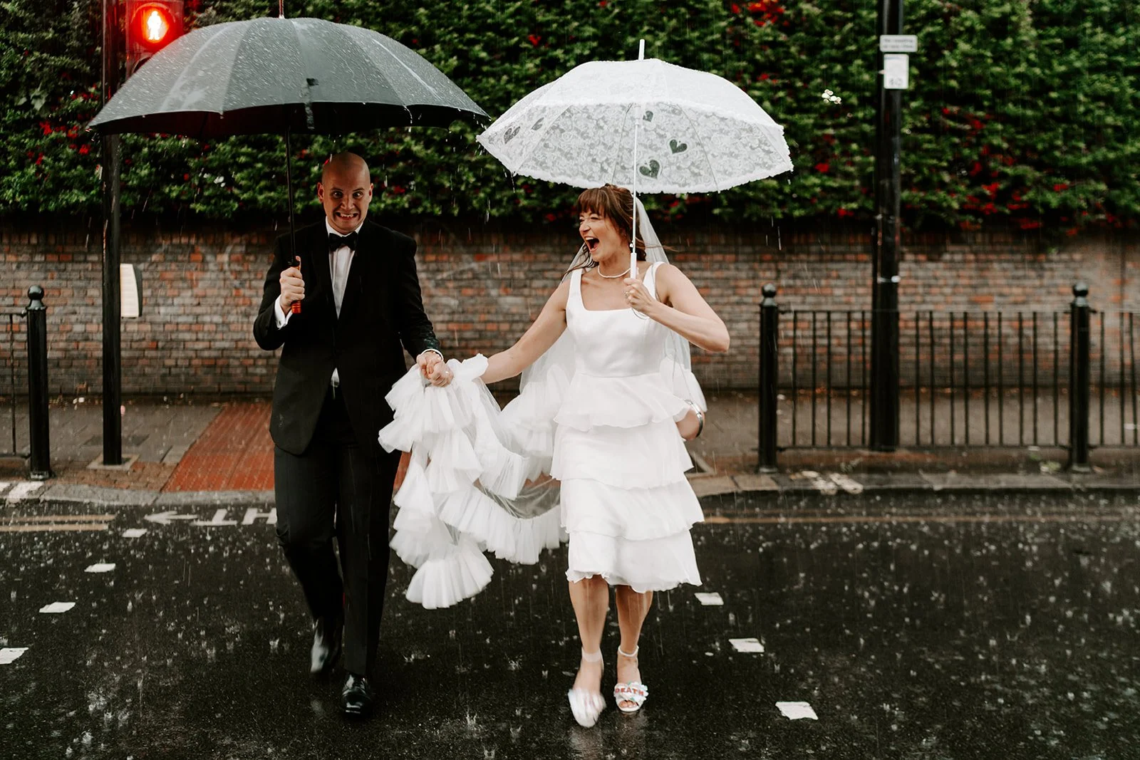 London town hall wedding couple crossing a city street in heavy rain with umbrellas, laughing together