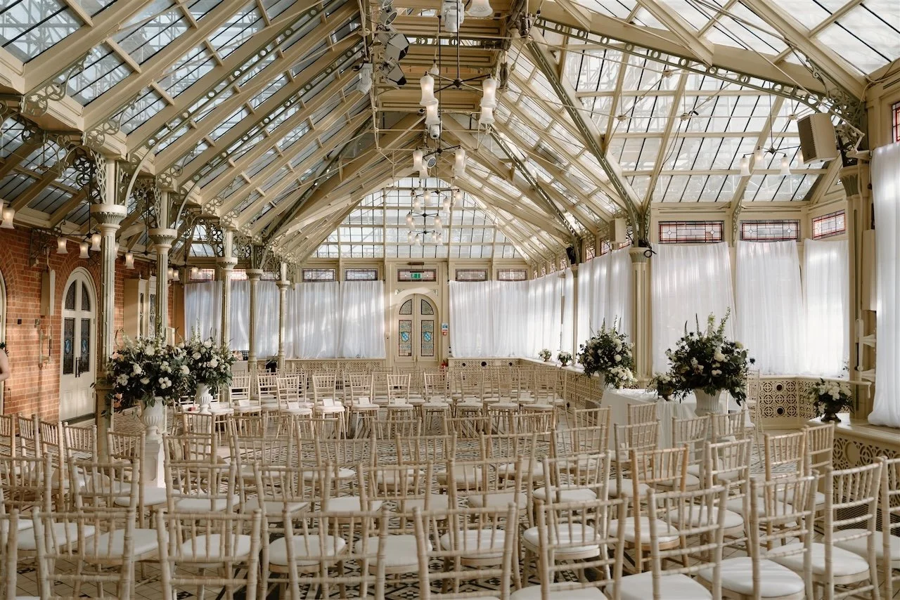 Ceremony setup inside the Kilworth House orangery with draped walls, floral arrangements, and a circular seating layout for a black tie wedding.