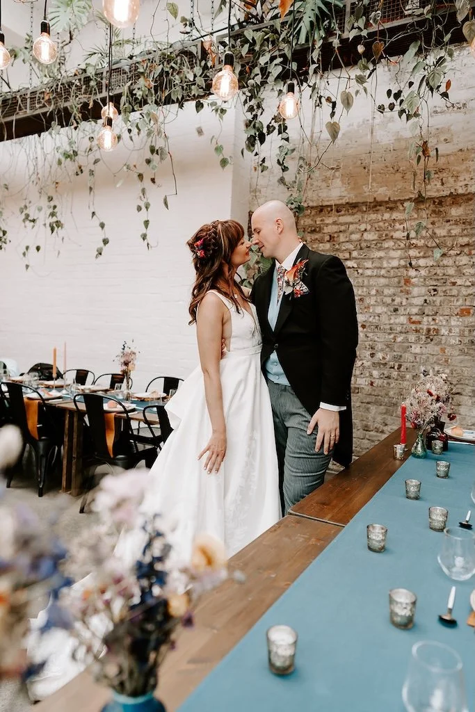 Bride and groom standing close together inside The Hackney wedding venue, surrounded by hanging plants, exposed brick and long dining tables in East London