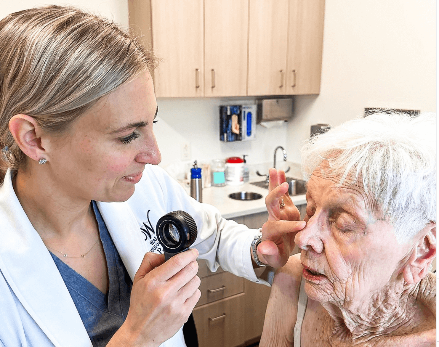 A healthcare professional examines an elderly woman's eye with a magnifying instrument in a clinic setting.