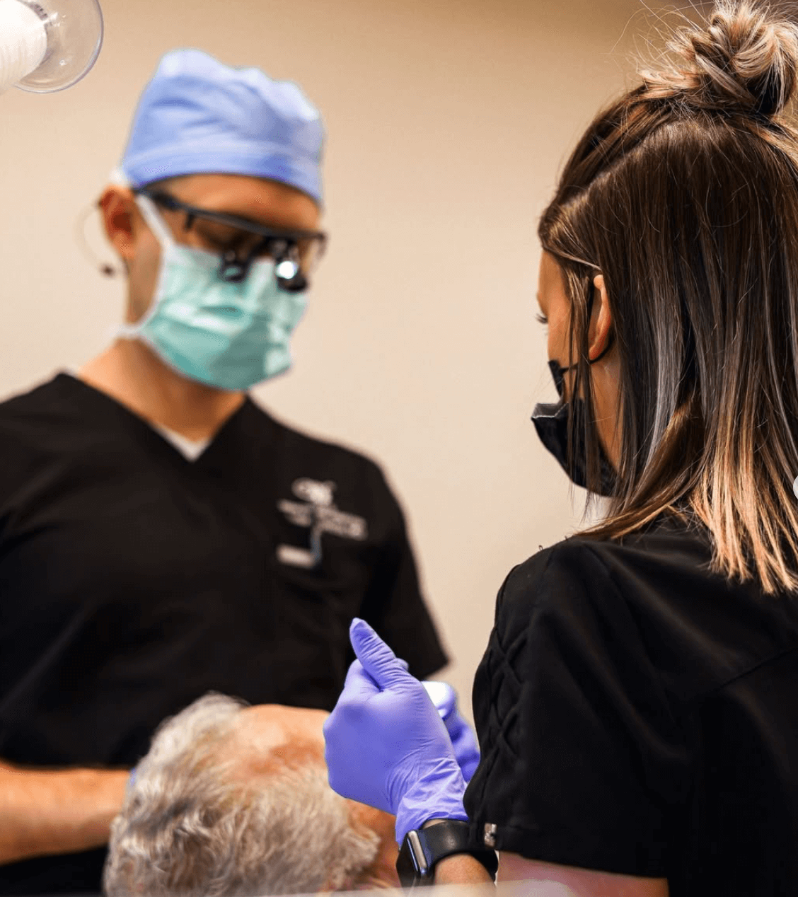 A healthcare professional administering a dental shot to a patient, both wearing masks, gloves, and protective clothing.