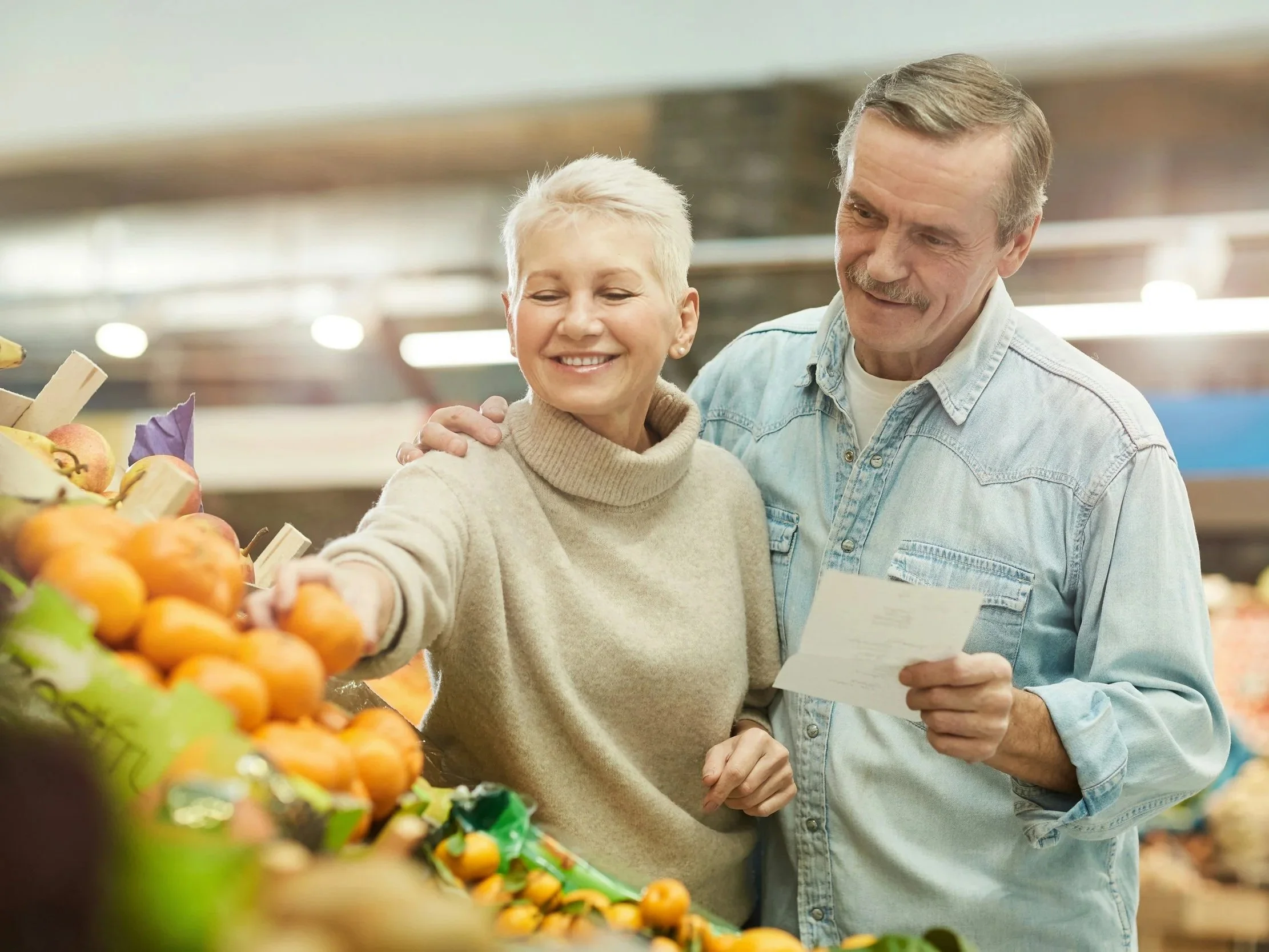 An older couple reaches for fruit while consulting their grocery list