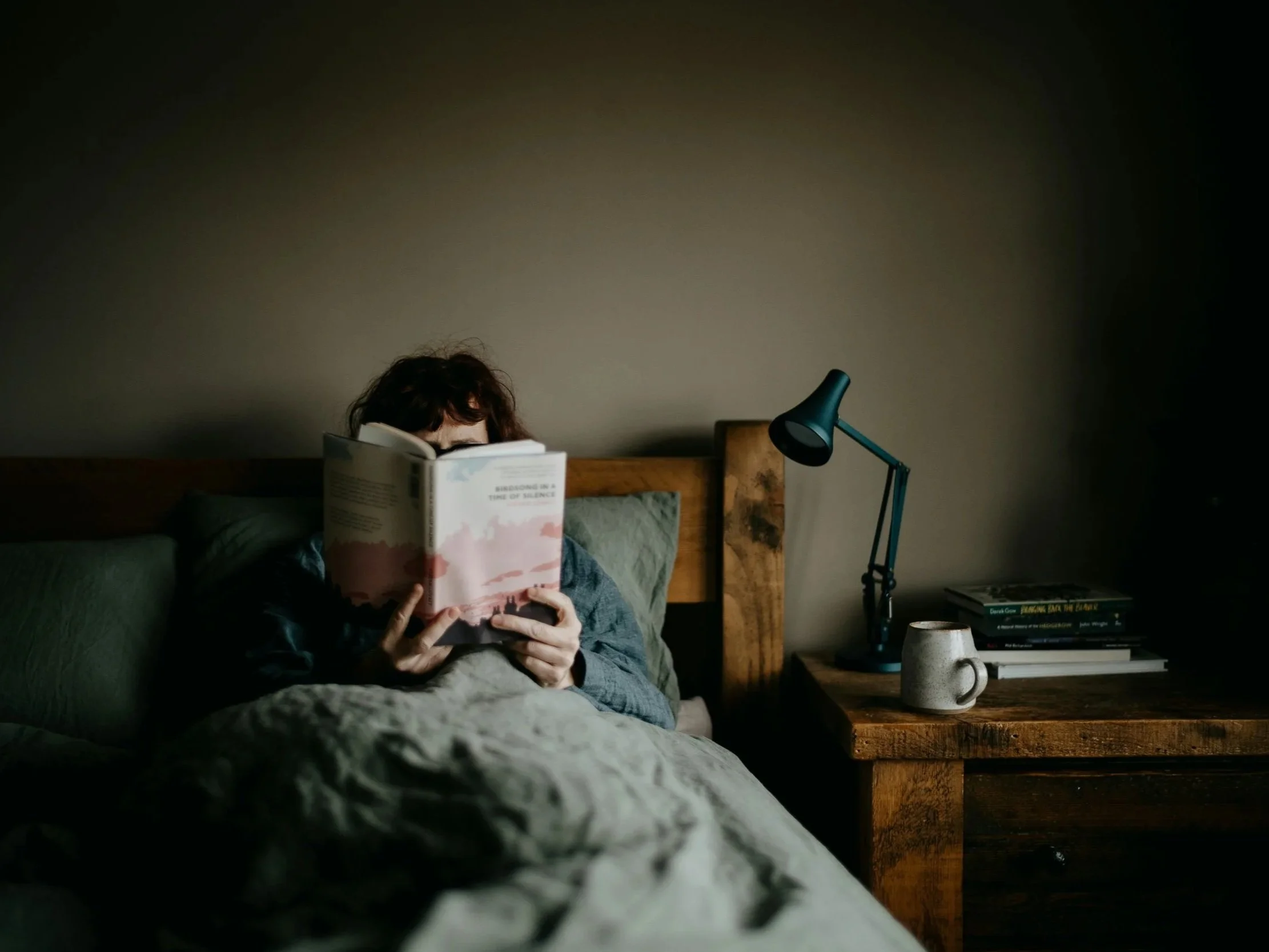 a woman sits in bed with a cup of tea and a book as part of her healthy bedtime routine