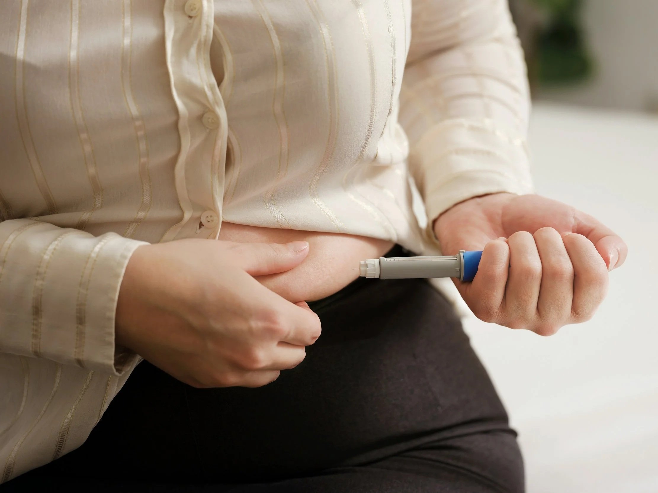 a close up of a woman's torso where she is pinching her stomach to administer the shot she holds in her other hand.
