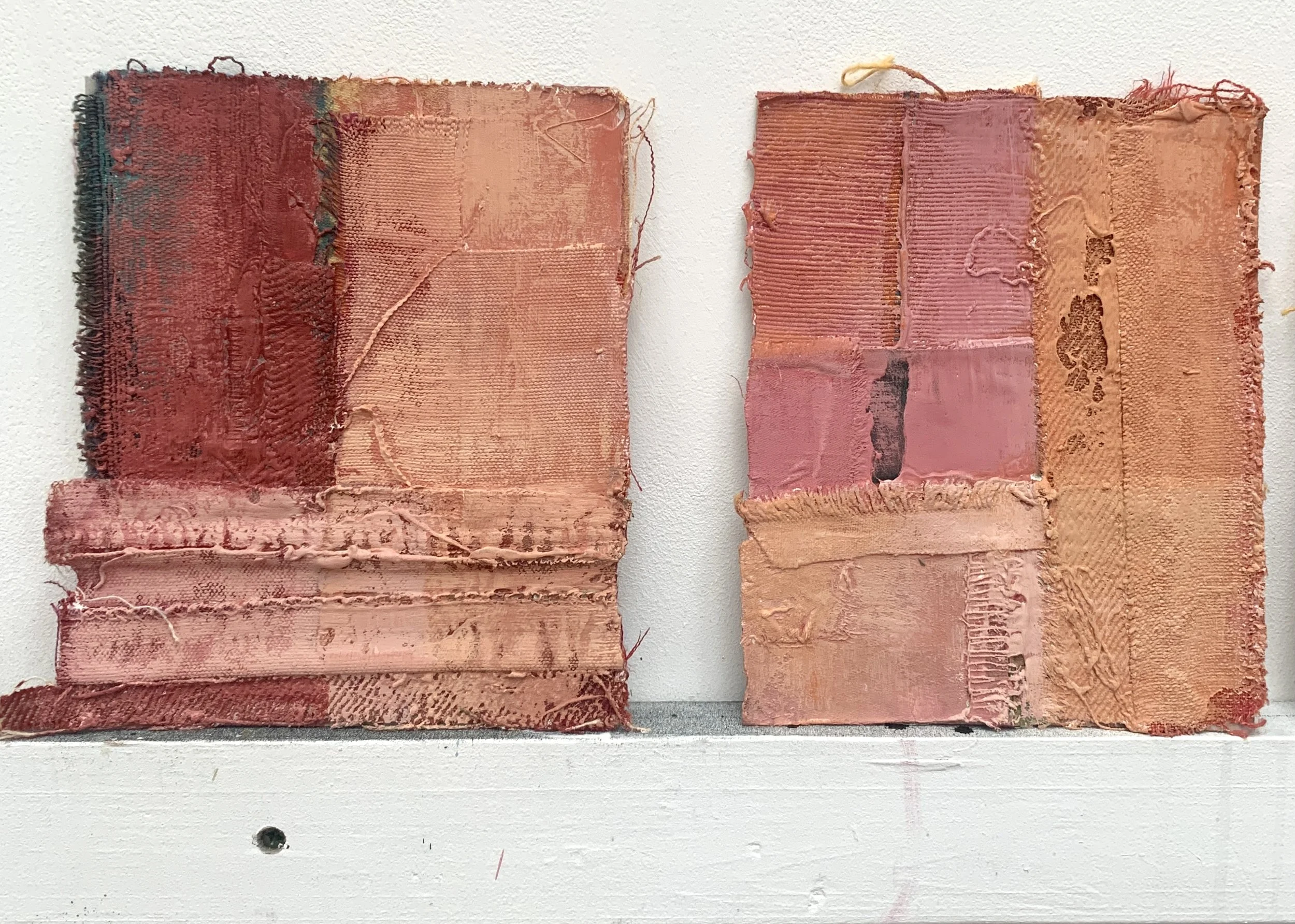 Two small abstract textile artworks in warm earthy colours displayed against a white wall, composed of layered paint, fabric and stitches