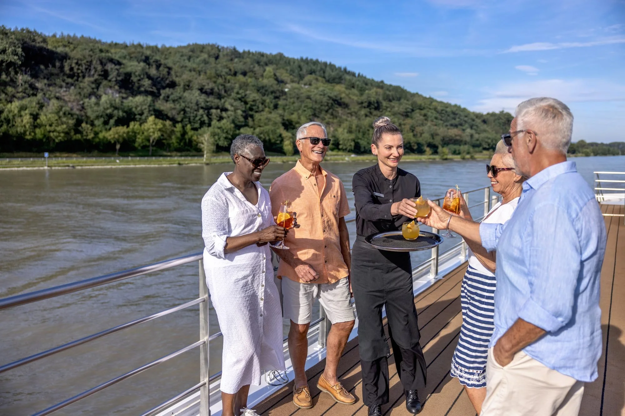 Couple of friends enjoying drinks on river cruise sun deck with scenic European landscape