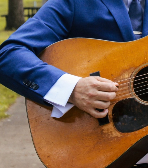 Person in a blue suit playing an acoustic guitar outdoors.