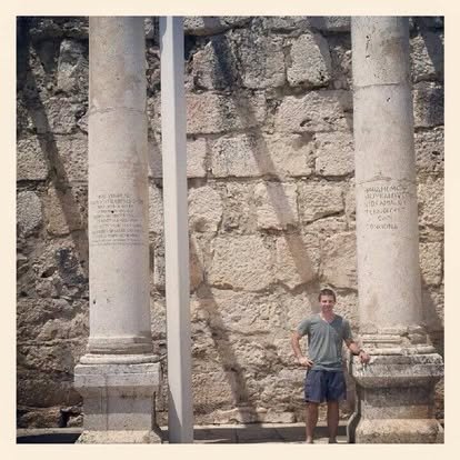 A man standing in front of ancient stone columns and a stone wall, with inscriptions on the columns.