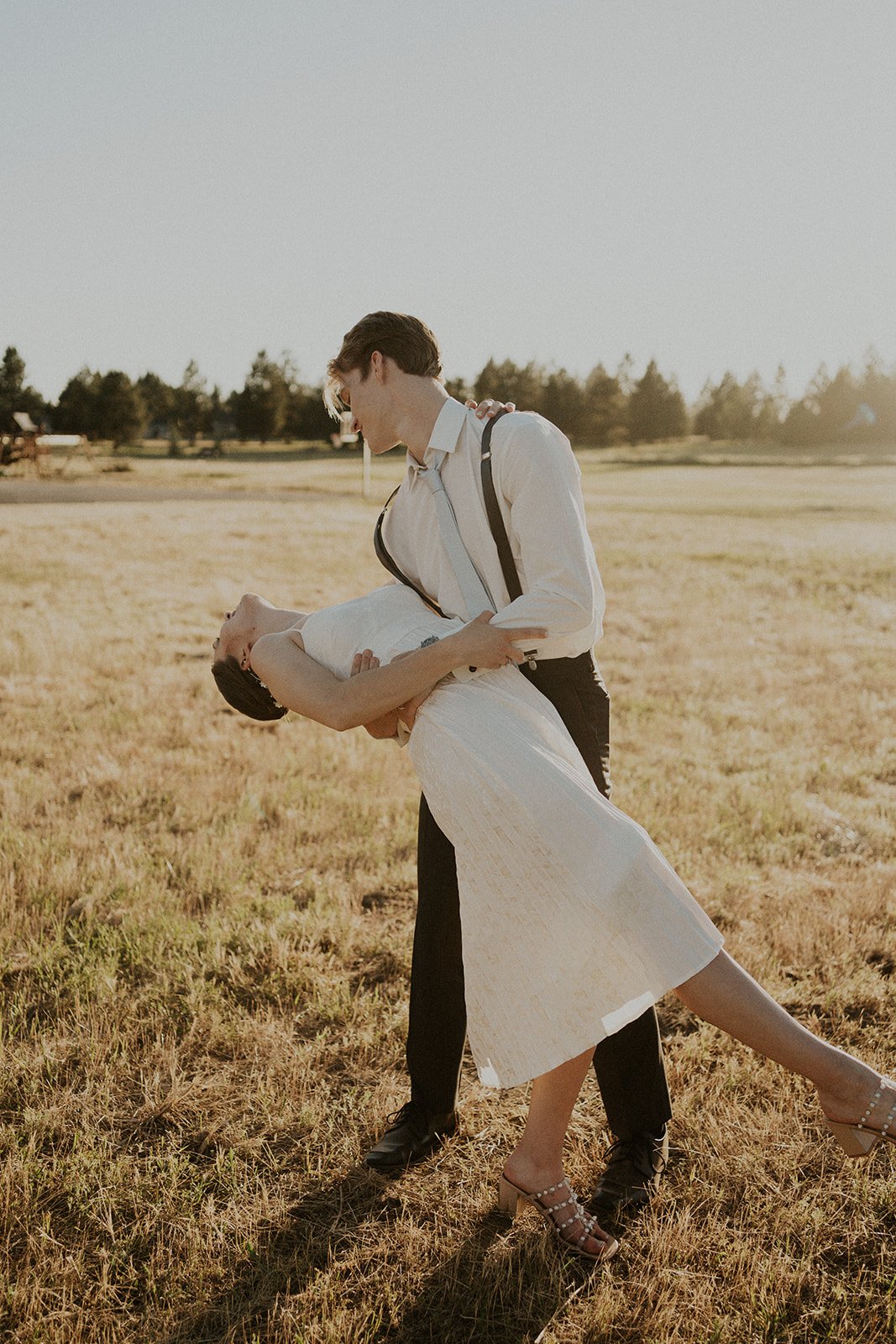 bride and groom dancing in field at sunset