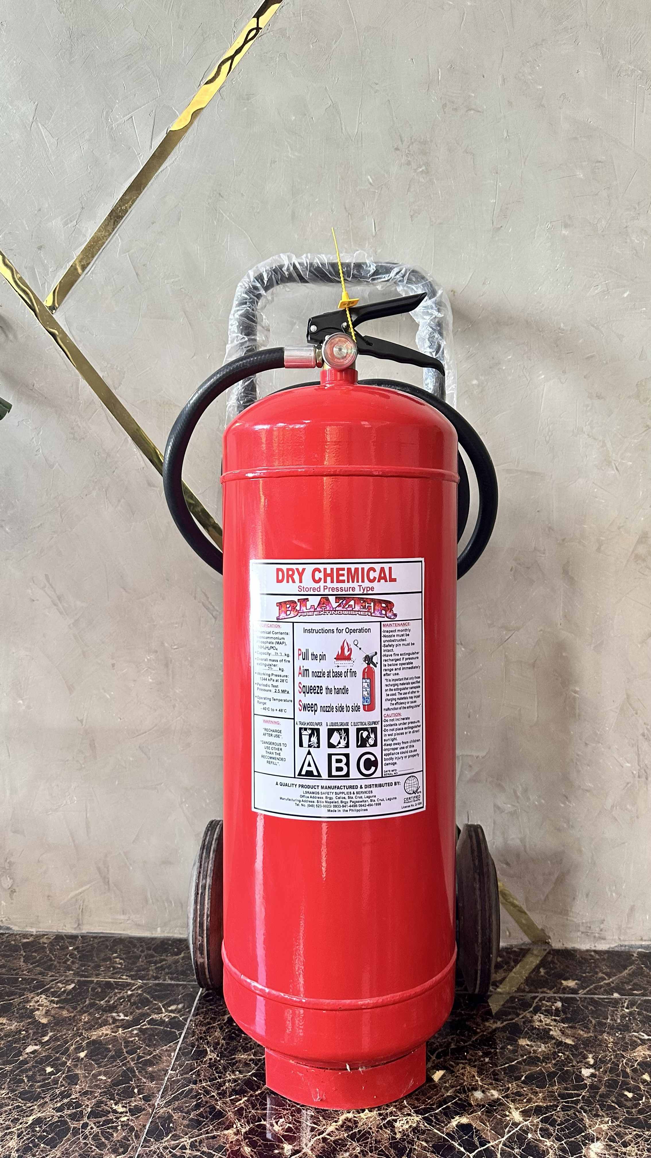 A red fire extinguisher mounted on a wall with a yellow pull pin and black handle, located on a marble floor.