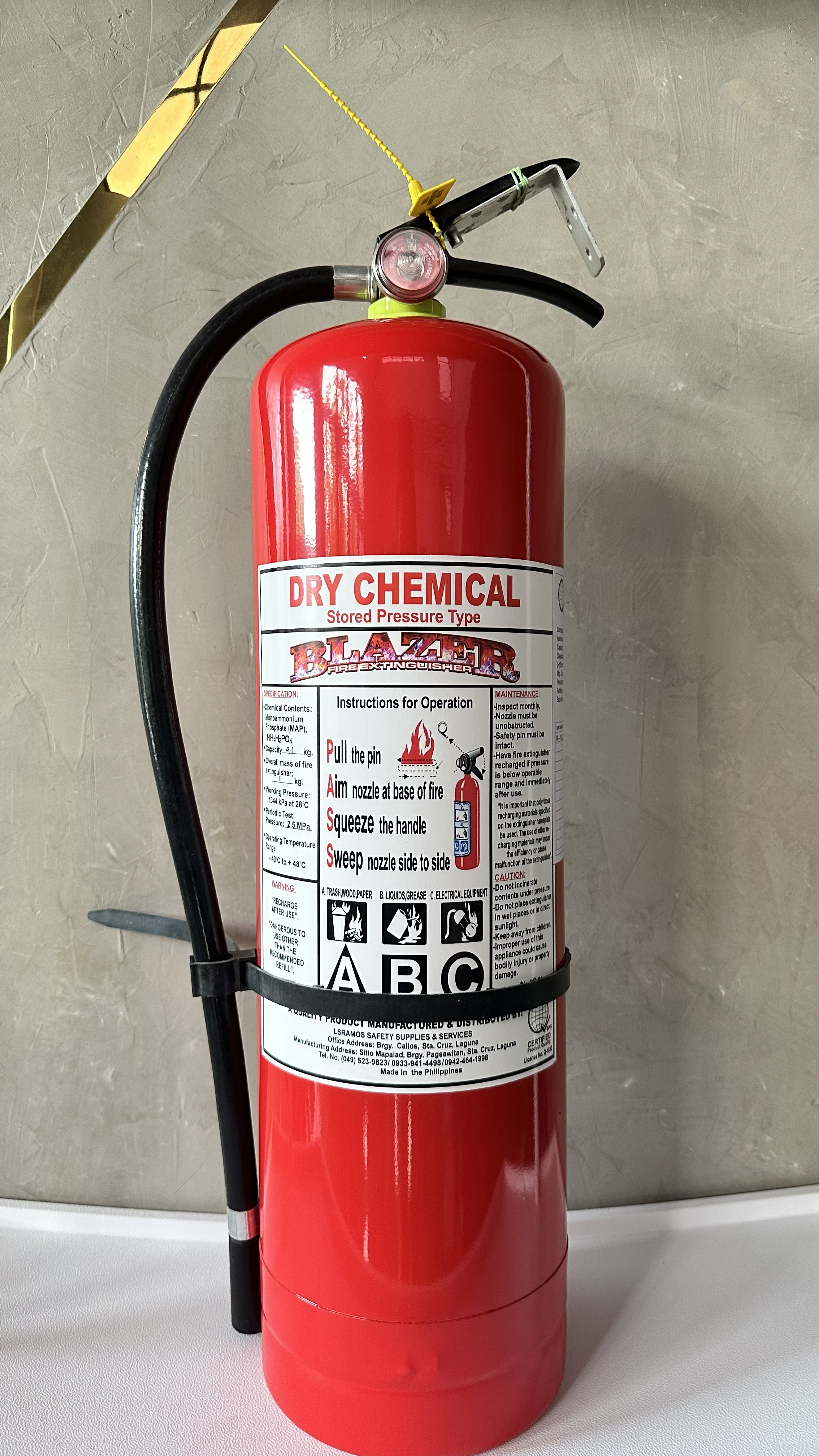 Red dry chemical fire extinguisher mounted on a wall, with a black hose and nozzle, and instructions for operation printed on the label.