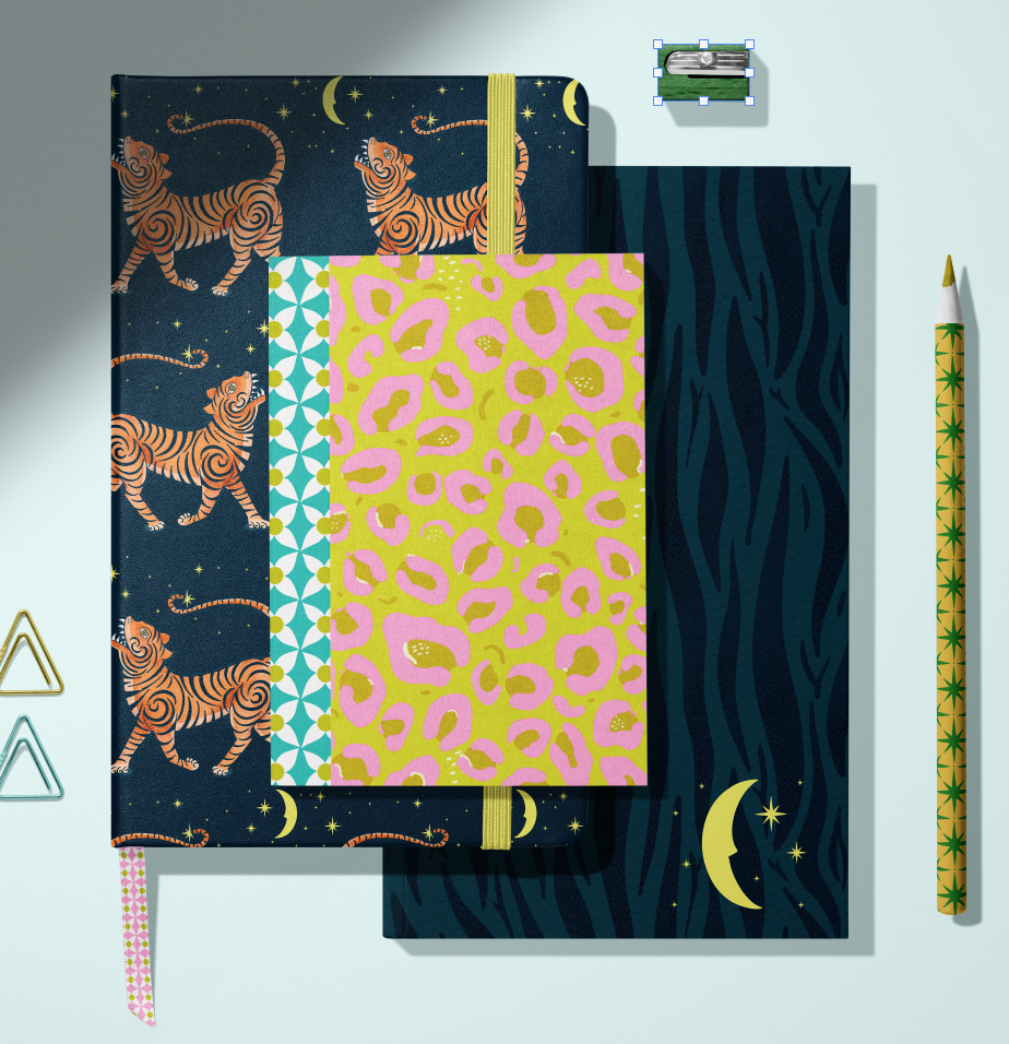 A collection of colorful notebooks with various patterns, including tigers on a dark starry night background, geometric shapes, a pink and yellow animal print, and blue zebra stripes. There is a yellow pen with a star pattern, a small stack of sticky notes, and paper clips nearby.