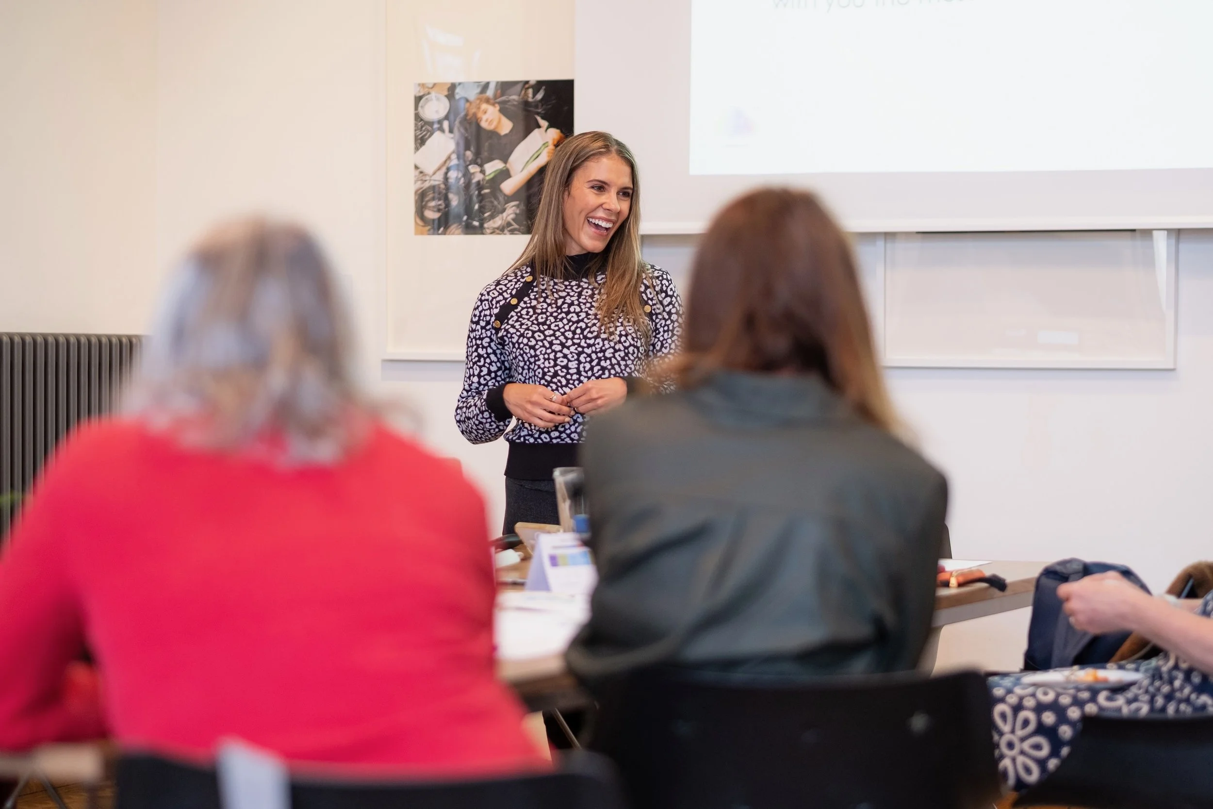 woman in a sweater laughing in front of a classroom