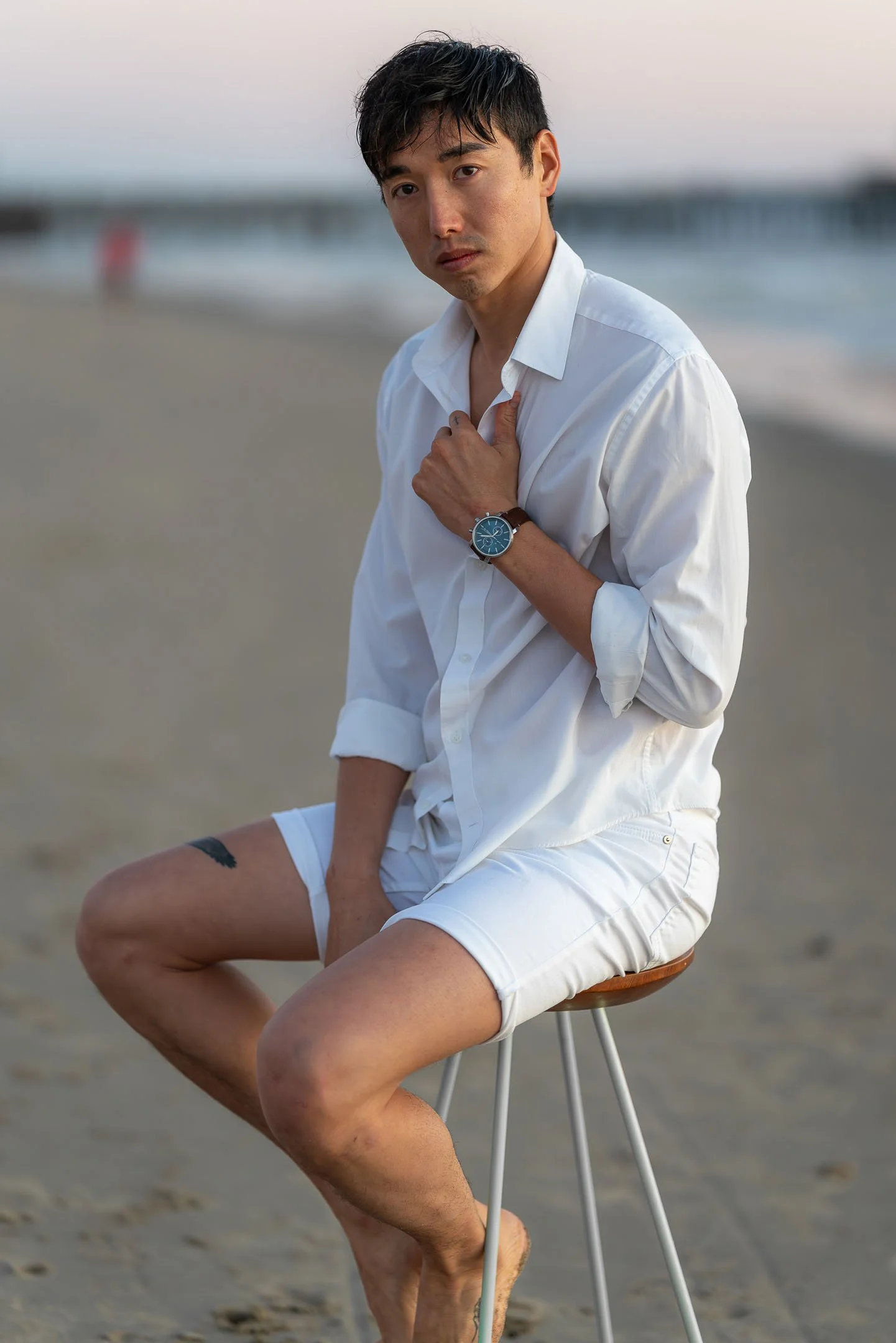Male model wearing white resortwear while posing on stool