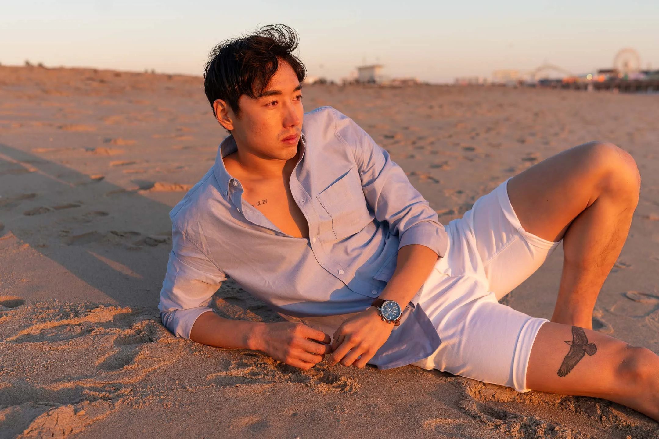 Male model lying on Santa Monica beach at sunset wearing blue watch