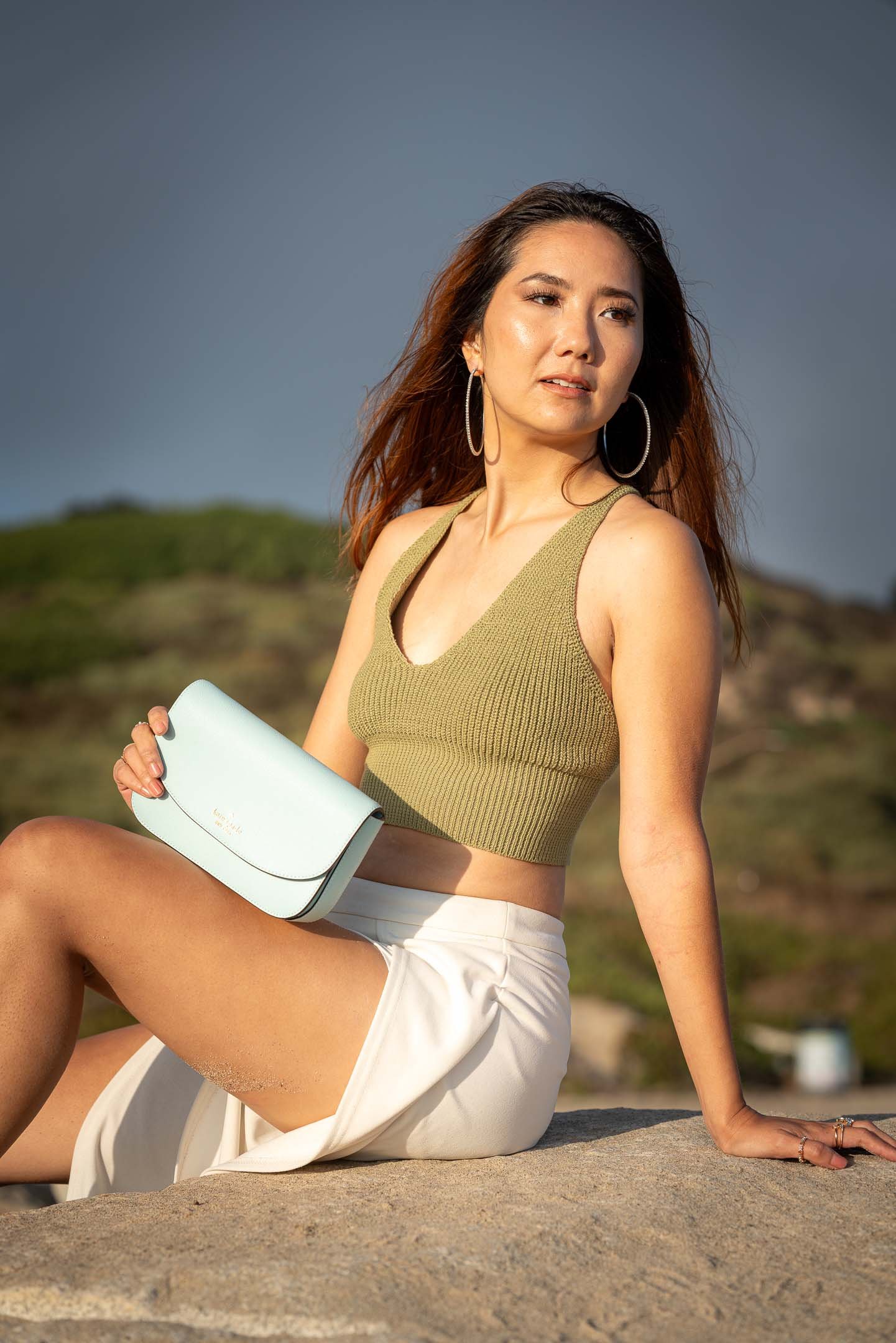 Los Angeles model posing with blue handbag sitting on the rocks at Santa Monica Beach