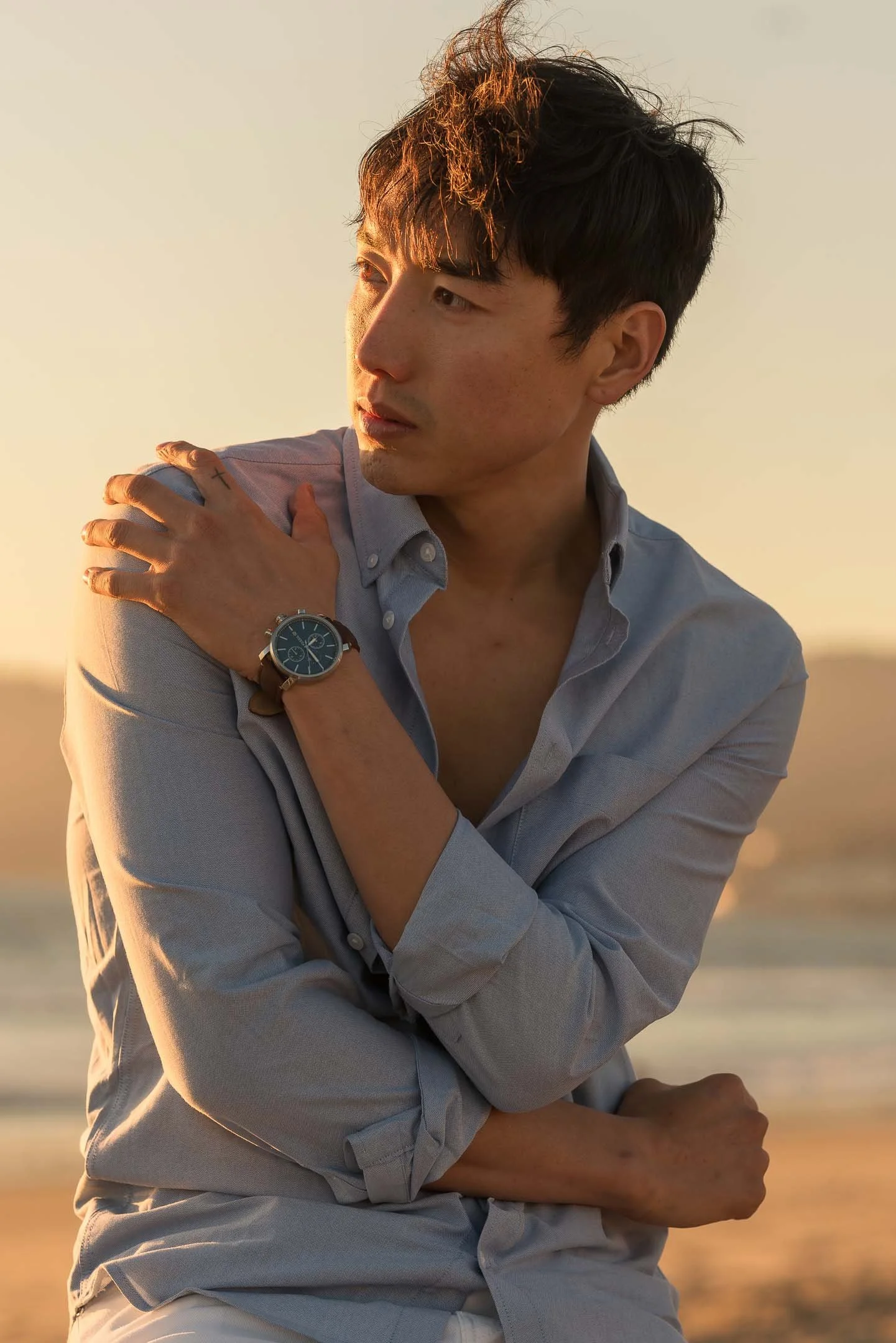 Male model posing at the beach wearing blue watch at sunset