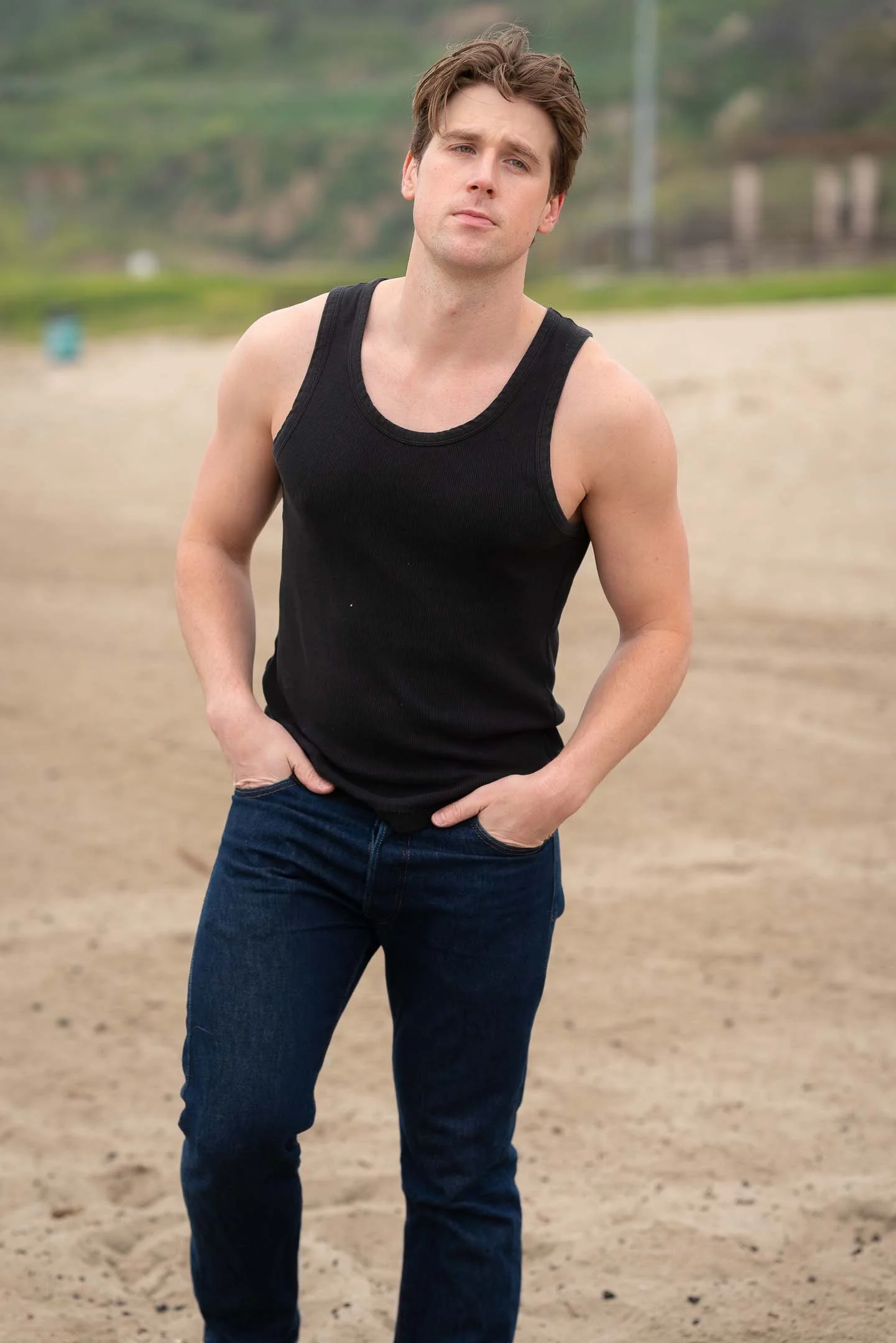 Male model wearing blue jeans and black top posing on the beach