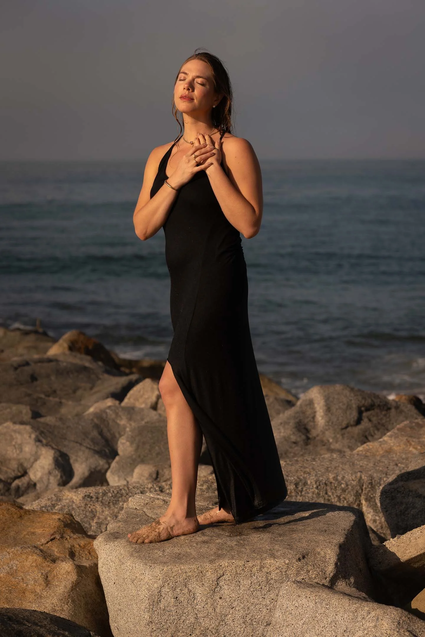 Model posing peacefully while standing on the rocks at sunrise