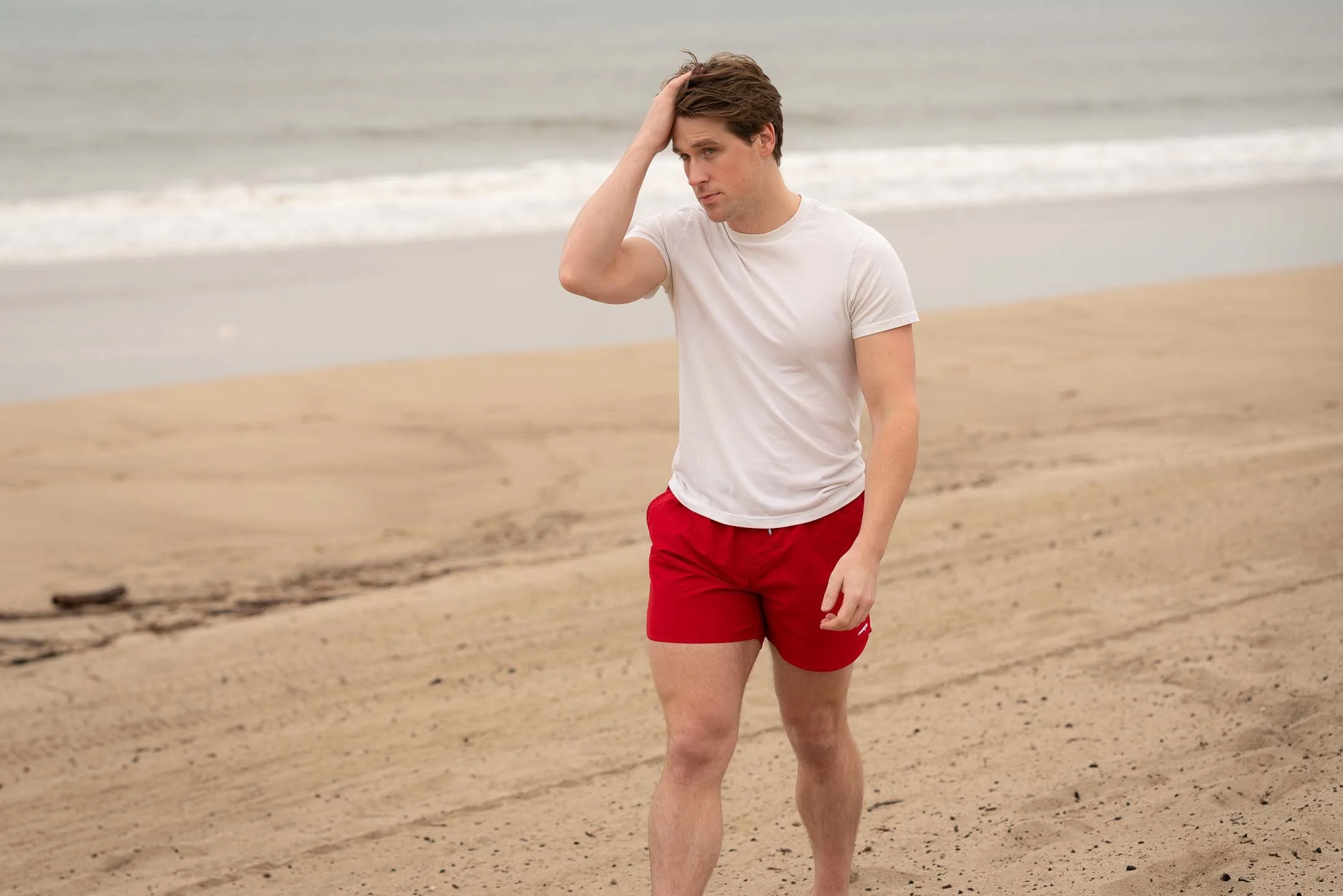 Male model walking on the beach wearing T-shirt and red swim trunks at the beach