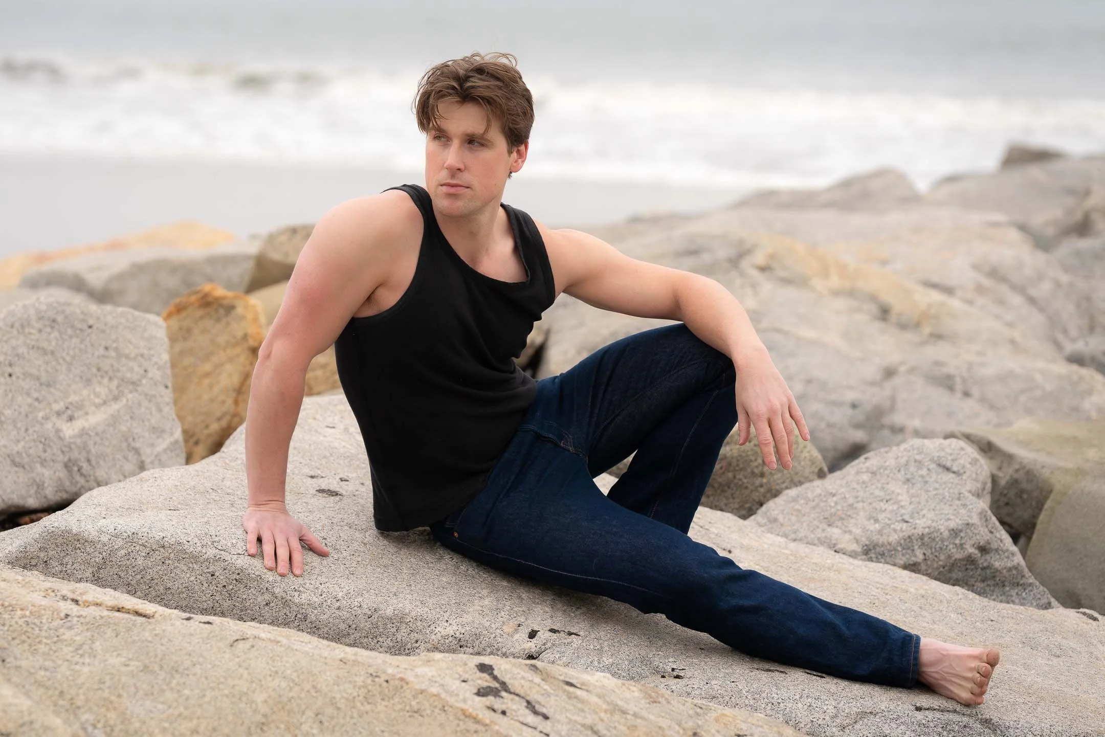 Male model sitting on the rocks at Santa Monica Beach during overcast evening
