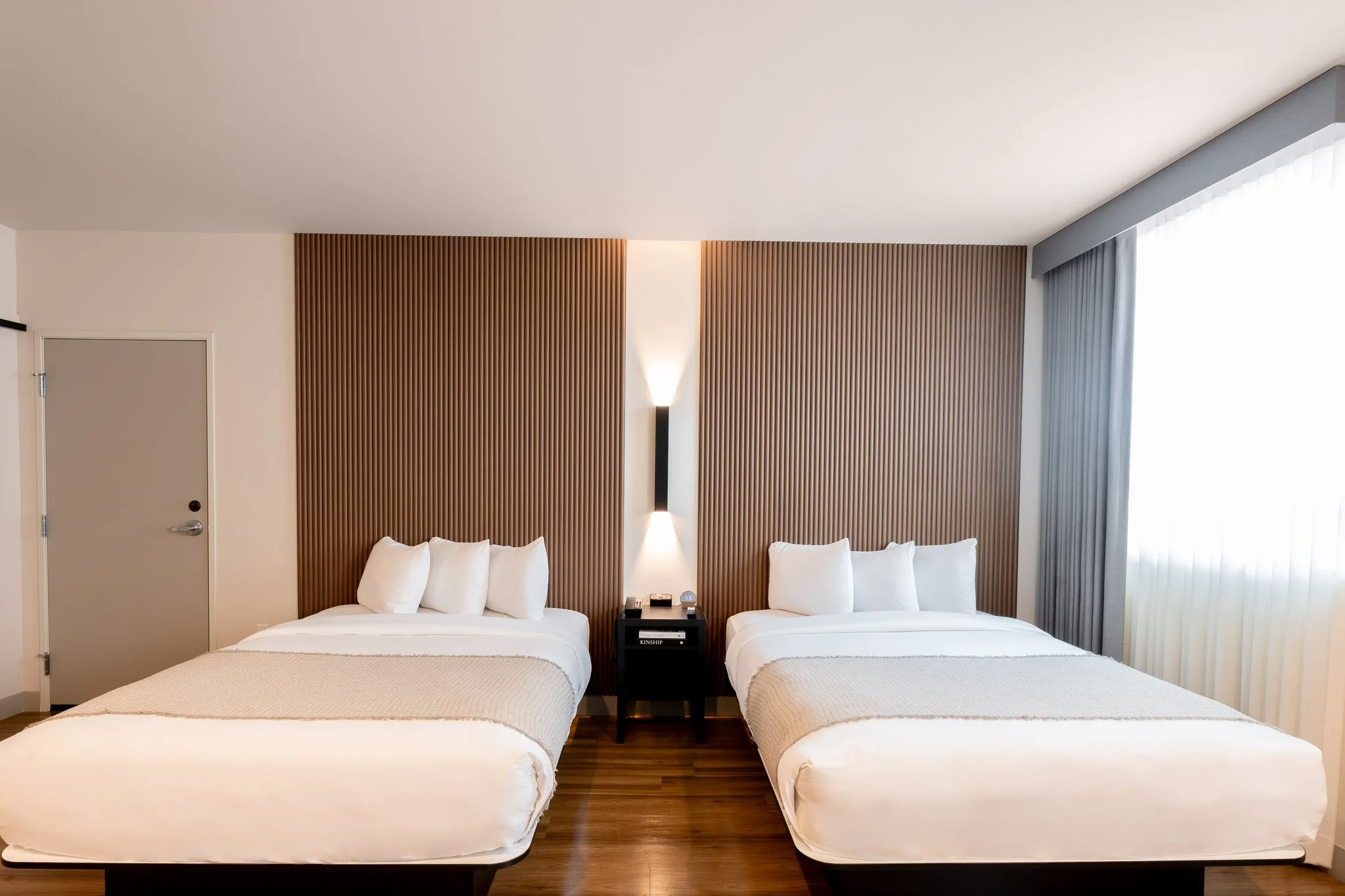 Two beds in a hotel room with a sconce light in Los Angeles