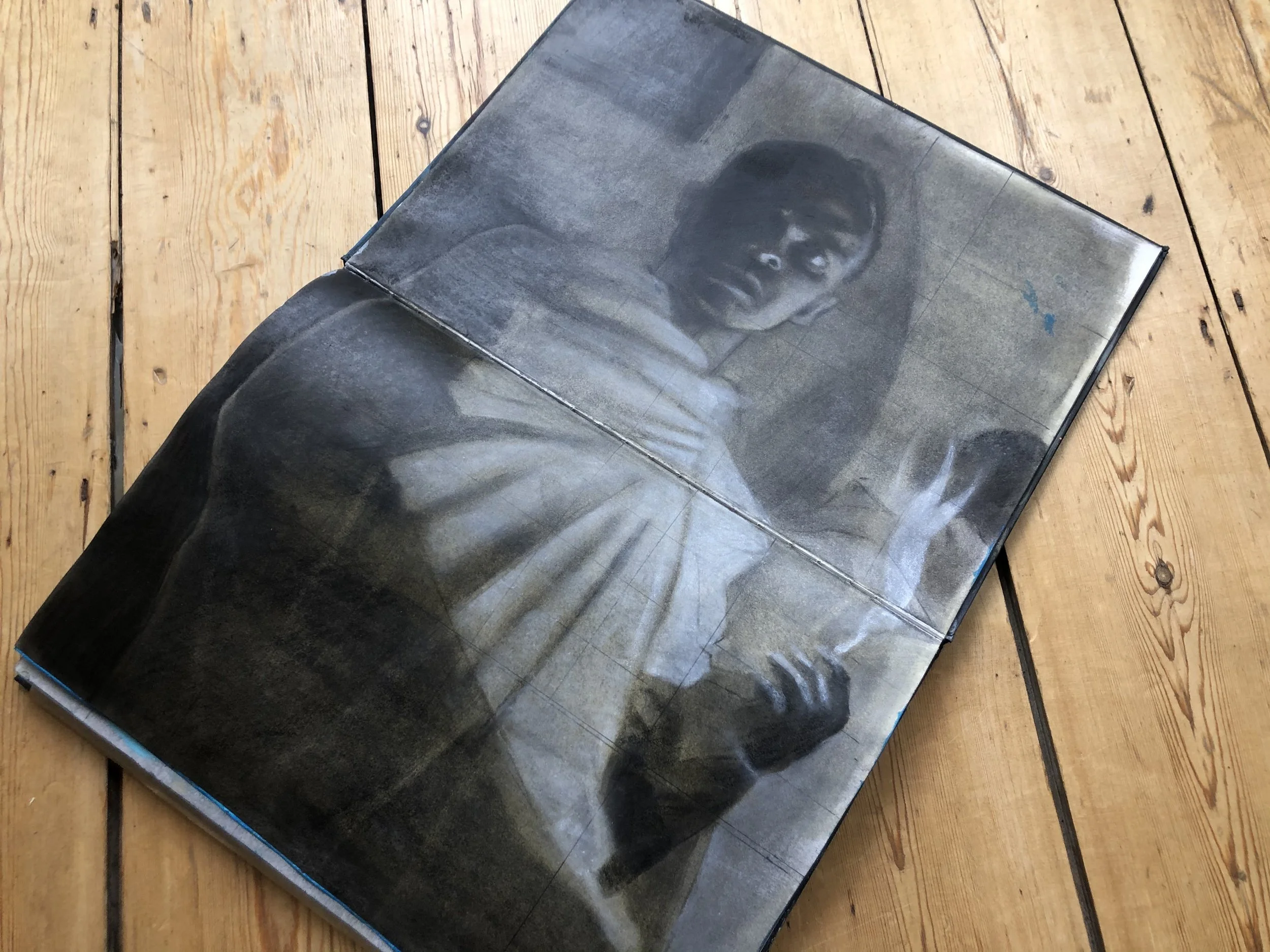 Open book with a grayscale portrait of a woman on the page lying on a wooden floor.