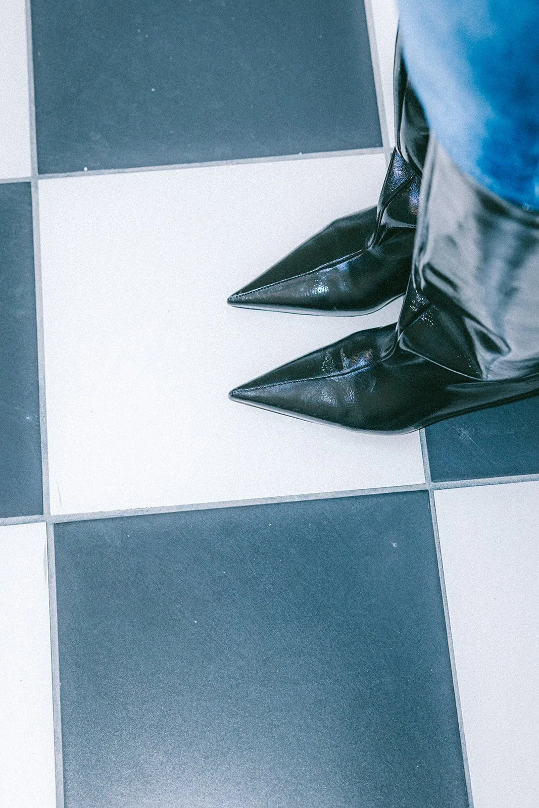 Close-up of black pointed-toe ankle boots worn by a person standing on a black-and-white checkered floor.