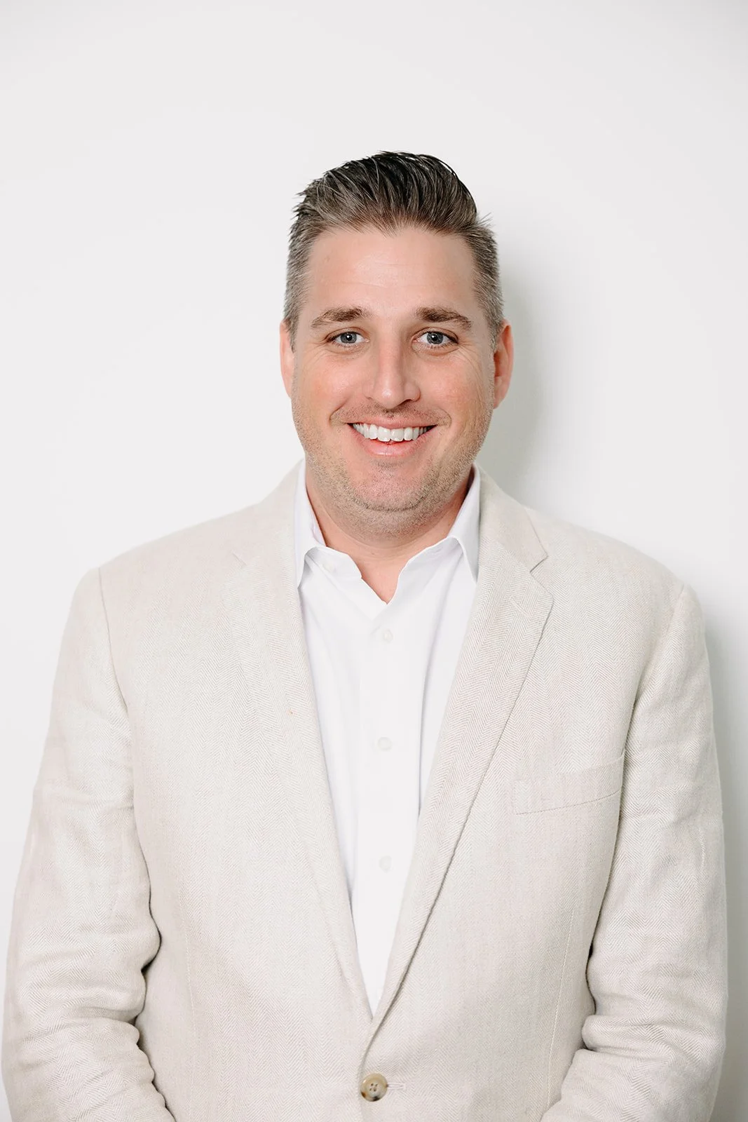Headshot of a smiling man in a light-colored blazer and white shirt standing against a white background.