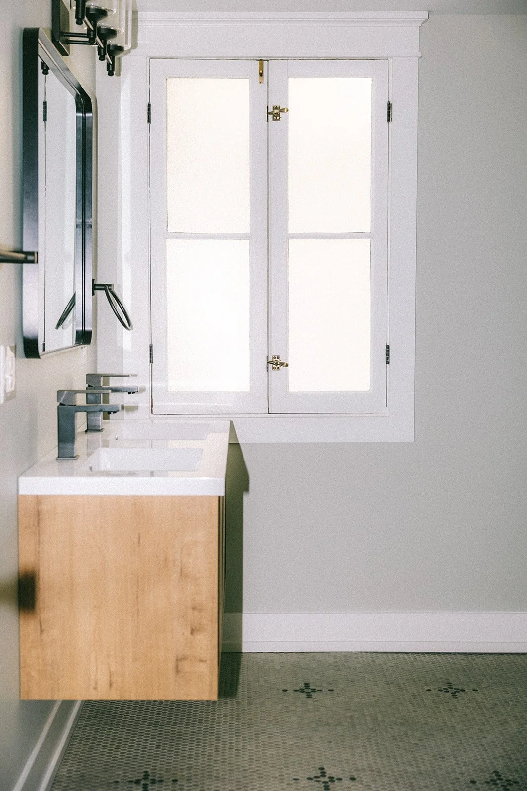 A minimalist bathroom with a white double window, a floating wooden vanity with a white sink, and a mosaic tile floor.