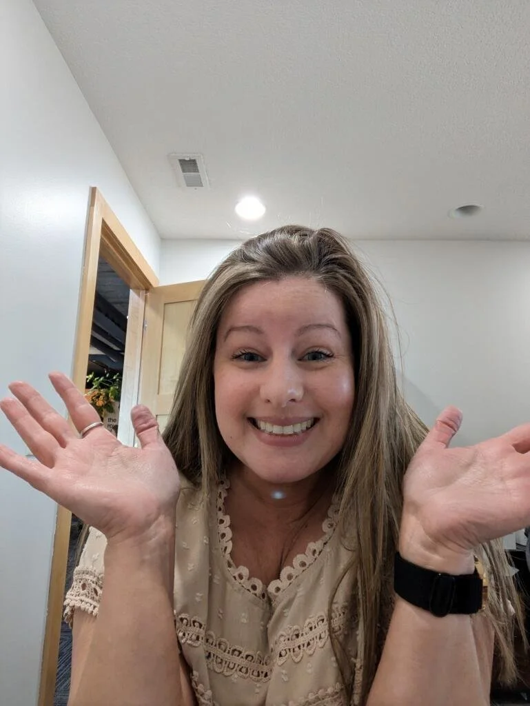 A woman smiling with her hands raised in a friendly gesture in an indoor setting.