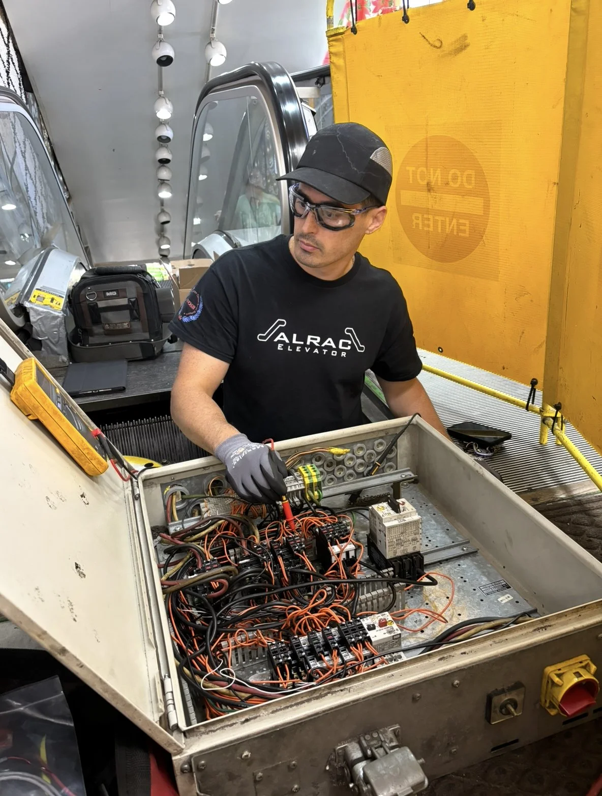 A technician working inside an elevator machine room, inspecting electrical components and wiring.