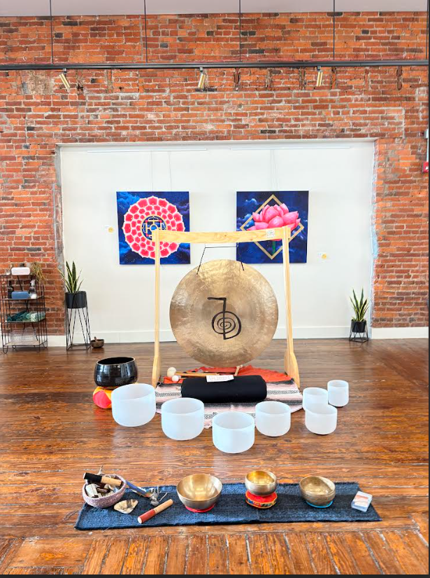 A flyer for a Full Moon Sound Bath event, featuring candles, stones, and bowls on the floor next to it.