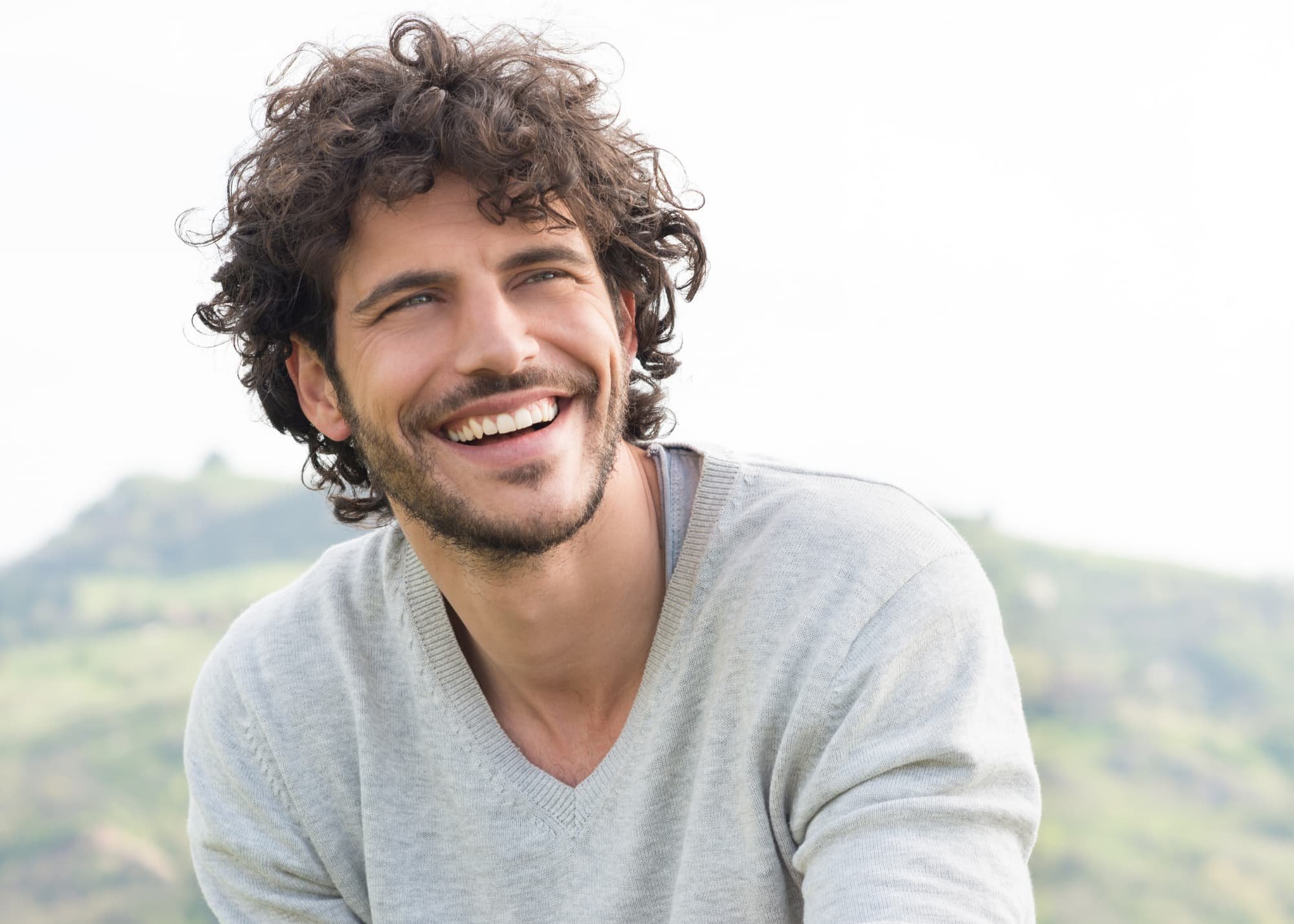 Man with curly hair smiling, wearing a grey sweater