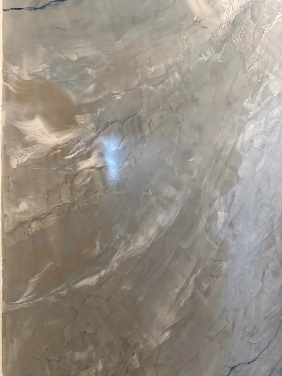 A smooth, shiny, gray marble wall with natural veining.