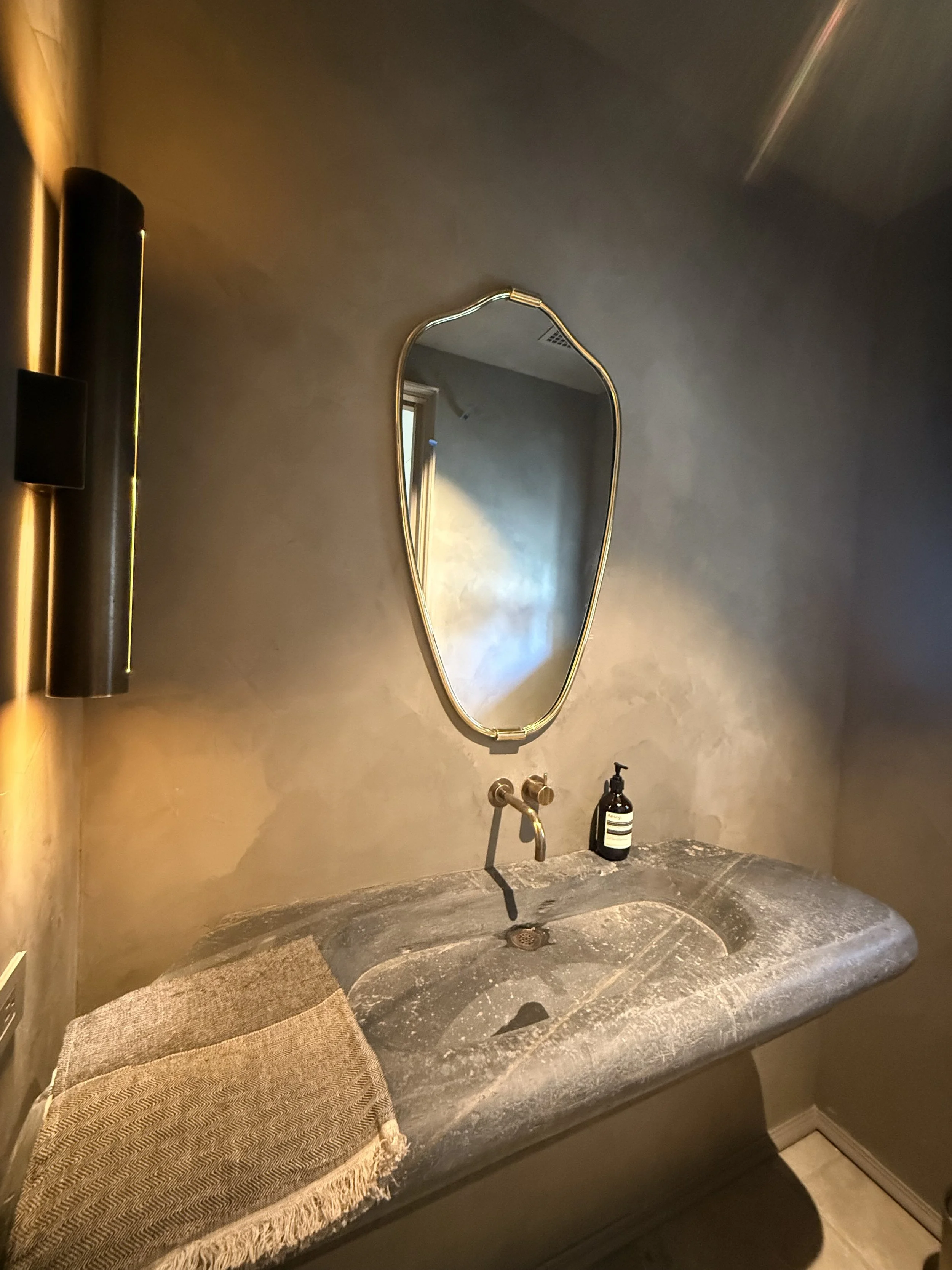 Bathroom sink with a mirror above and a beige towel on the left side. A soap dispenser is on the right side of the sink, and there is a black wall-mounted light fixture to the left.