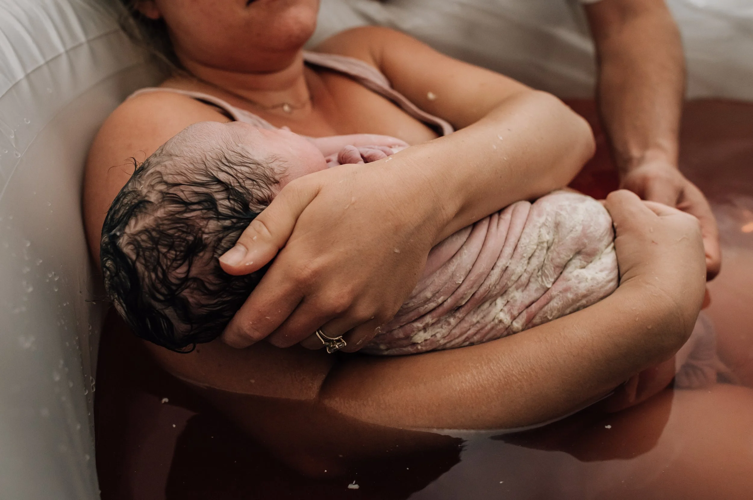 A woman breastfeeding a newborn baby in a bathtub.